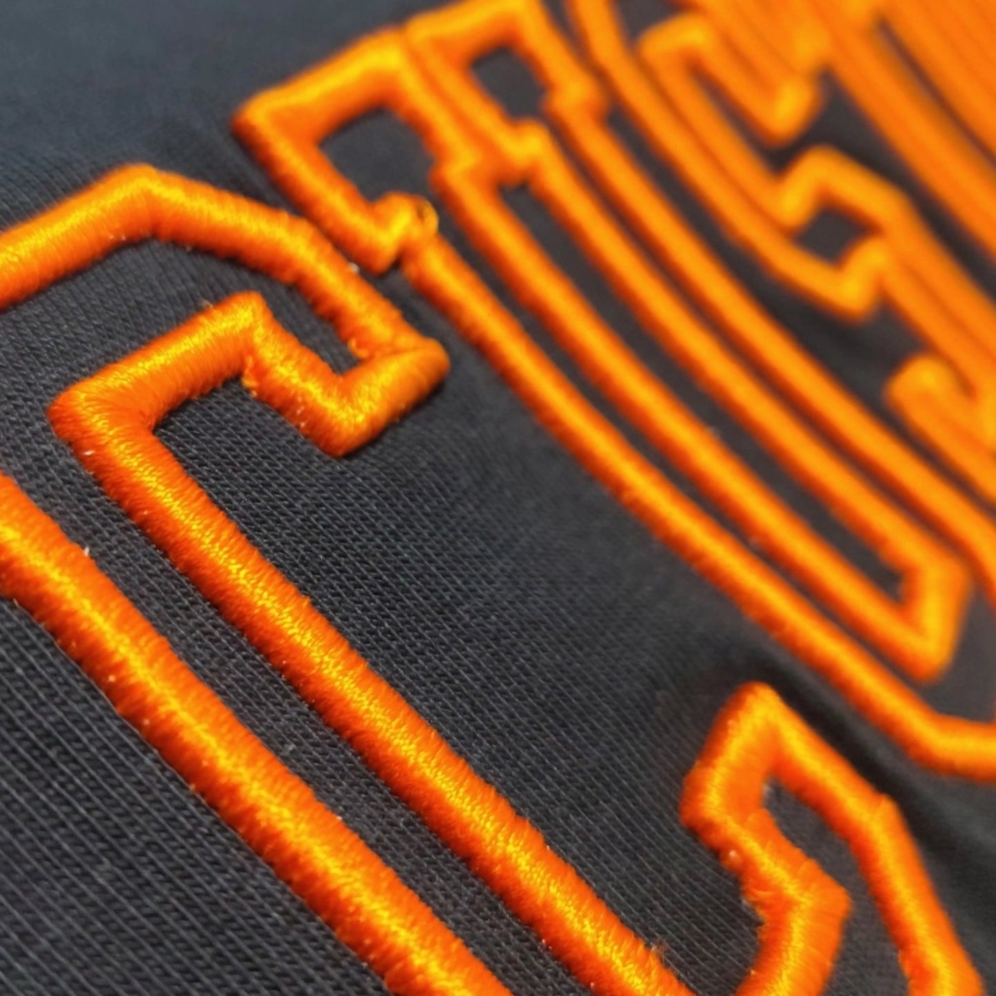 Close-up of 3D outline machine embroidery in orange thread on black tee — Embroidist