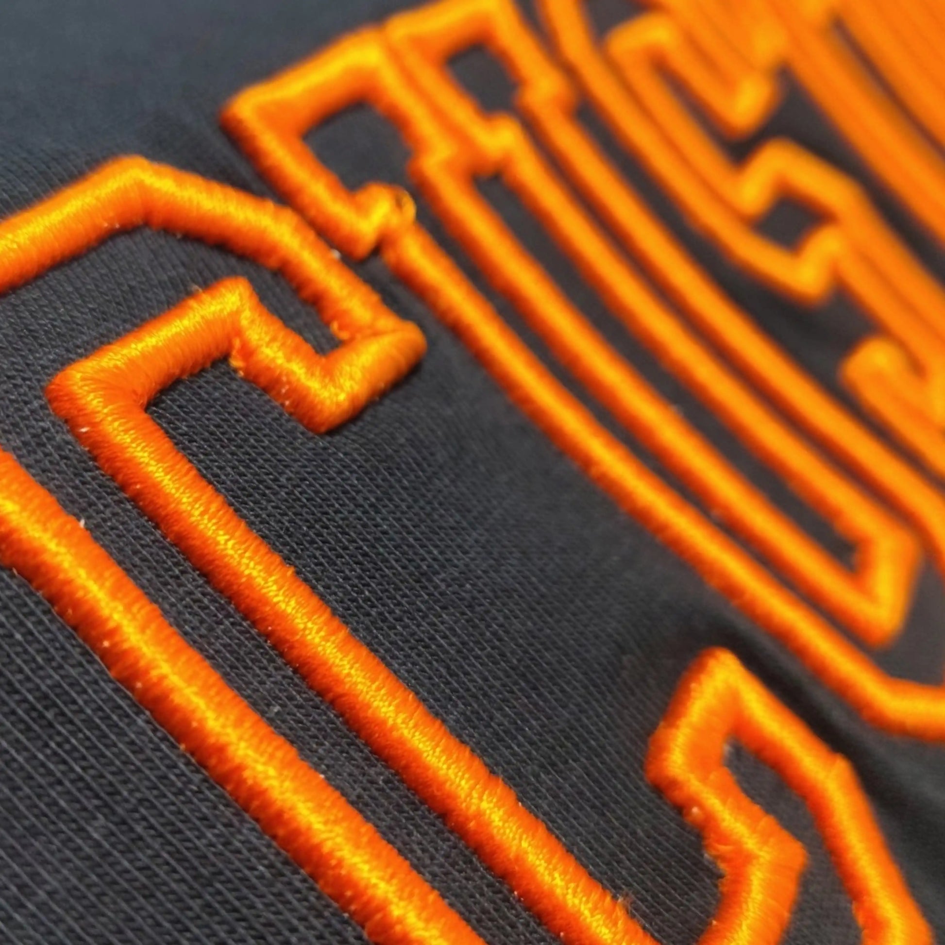 Close-up of 3D outline machine embroidery in orange thread on black tee — Embroidist