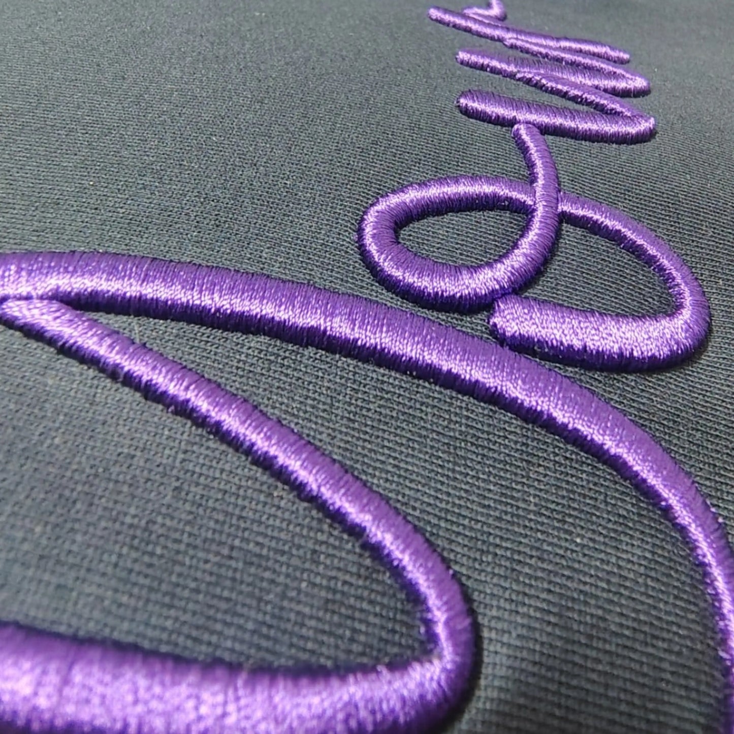 Close-up of 3D puff embroidery on custom t-shirt – raised violet satin-stitch threadwork