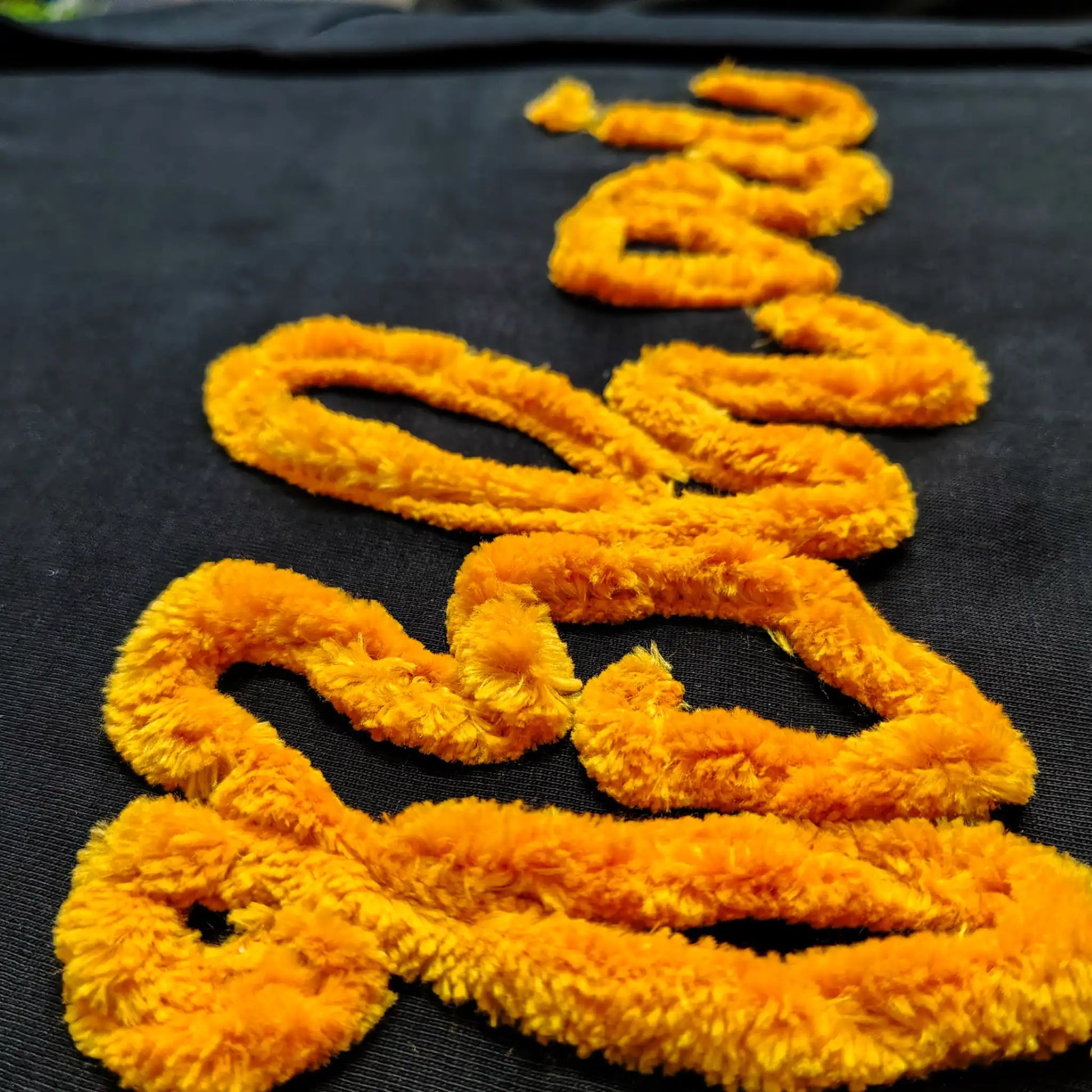 Macro close-up of marigold yellow chenille "Bhai" embroidery on black fabric — thick fluffy textured thread showing individual fibres, by Embroidist.