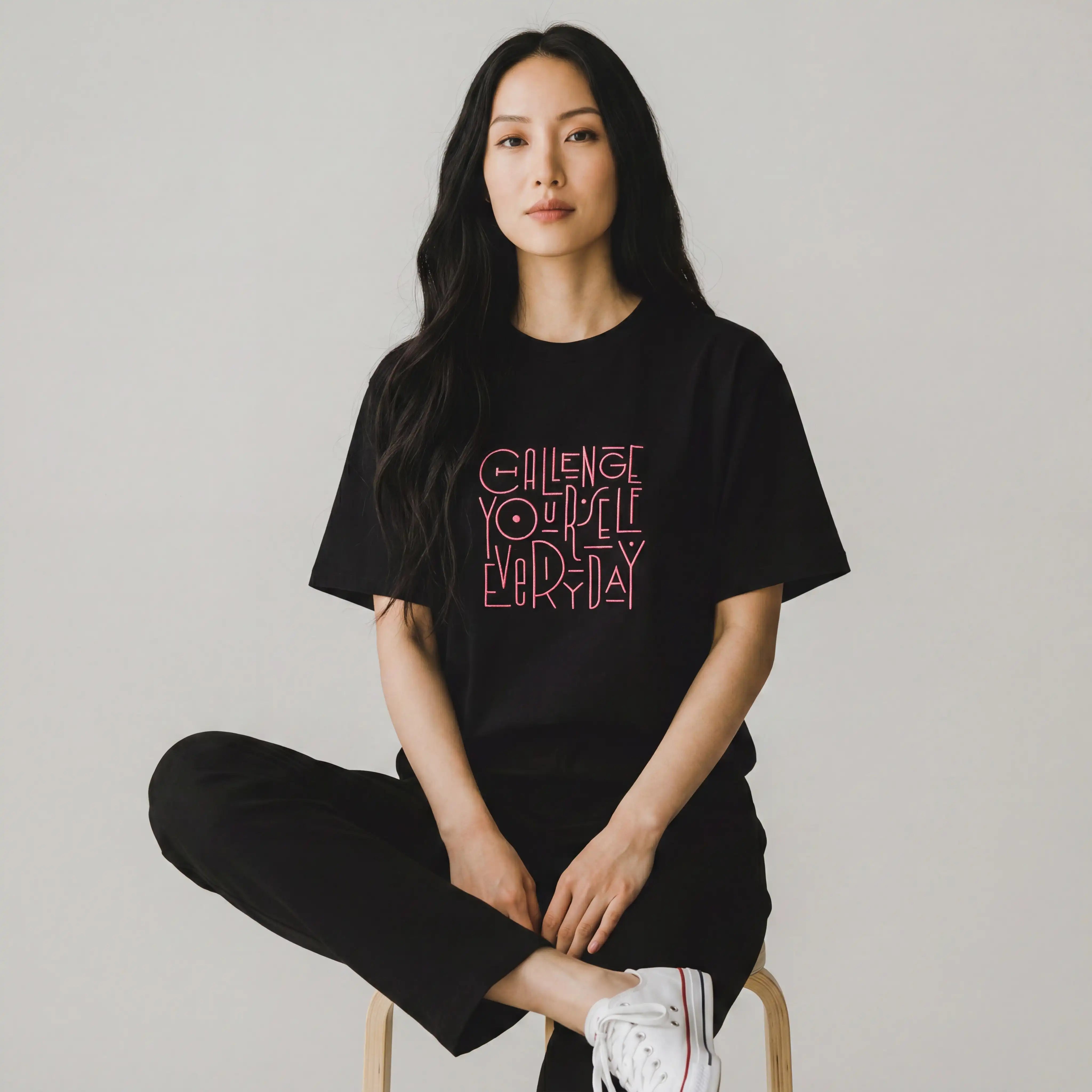 Woman wearing black oversized t-shirt with pink Challenge Yourself Everyday embroidery