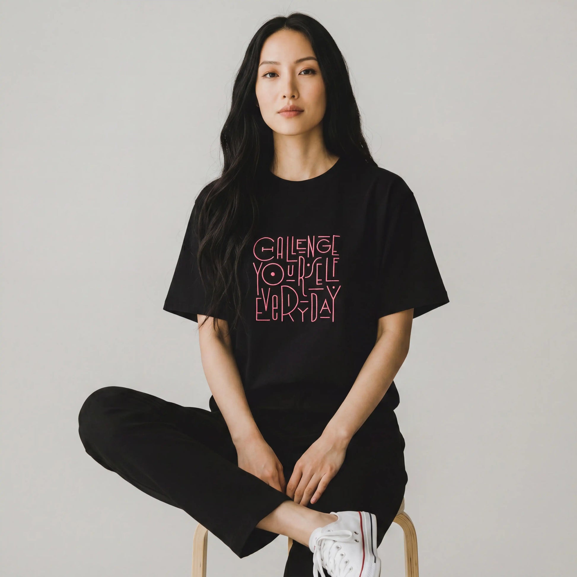 Woman wearing black oversized t-shirt with pink Challenge Yourself Everyday embroidery
