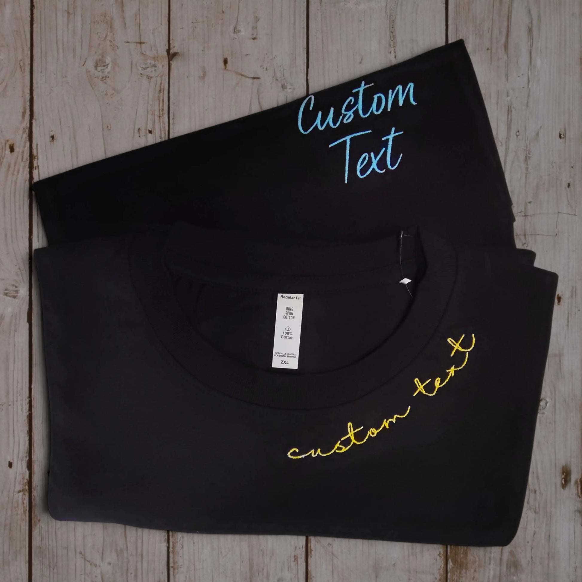 Black embroidered name tee folded — custom neckline script in yellow thread