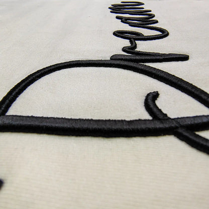 Extreme close-up of 3D puff embroidery thread detail on cream fabric — black raised cursive stitch showing depth, shadow and texture of Dream tee, by Embroidist