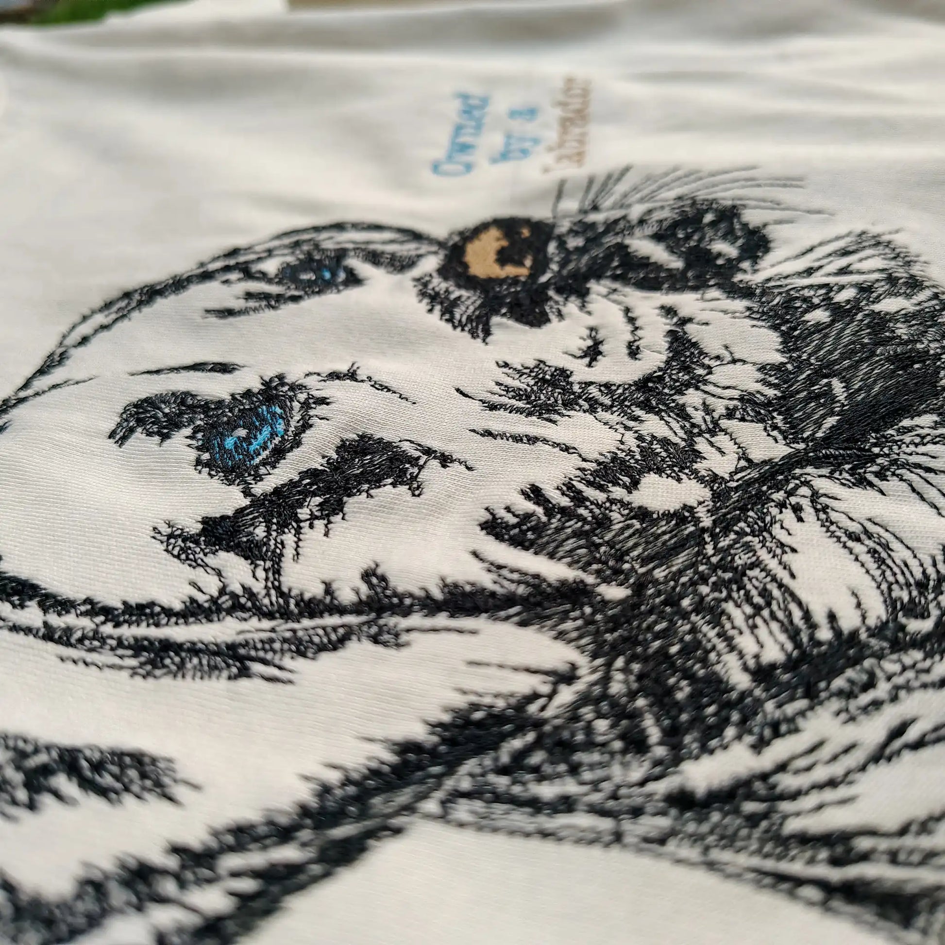 Angled detail shot of Labrador embroidery and ice blue Owned by a Labrador text on cream tee — Embroidist