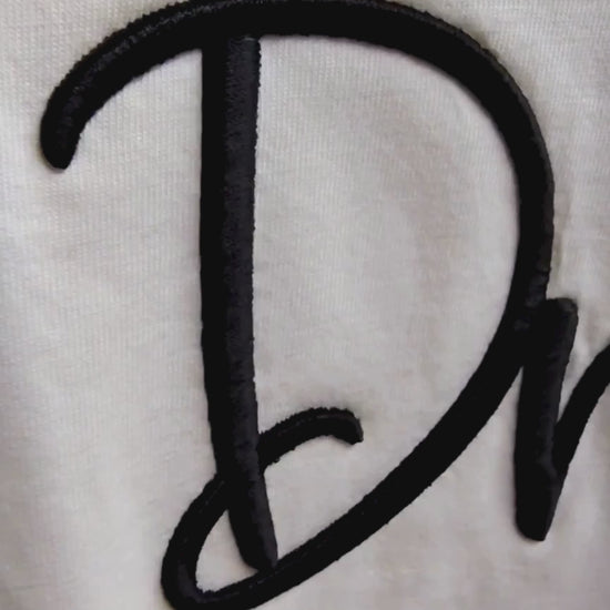 Video of 3D puff Dream embroidery detail — black raised cursive thread on cream fabric showing depth and texture, by Embroidist.