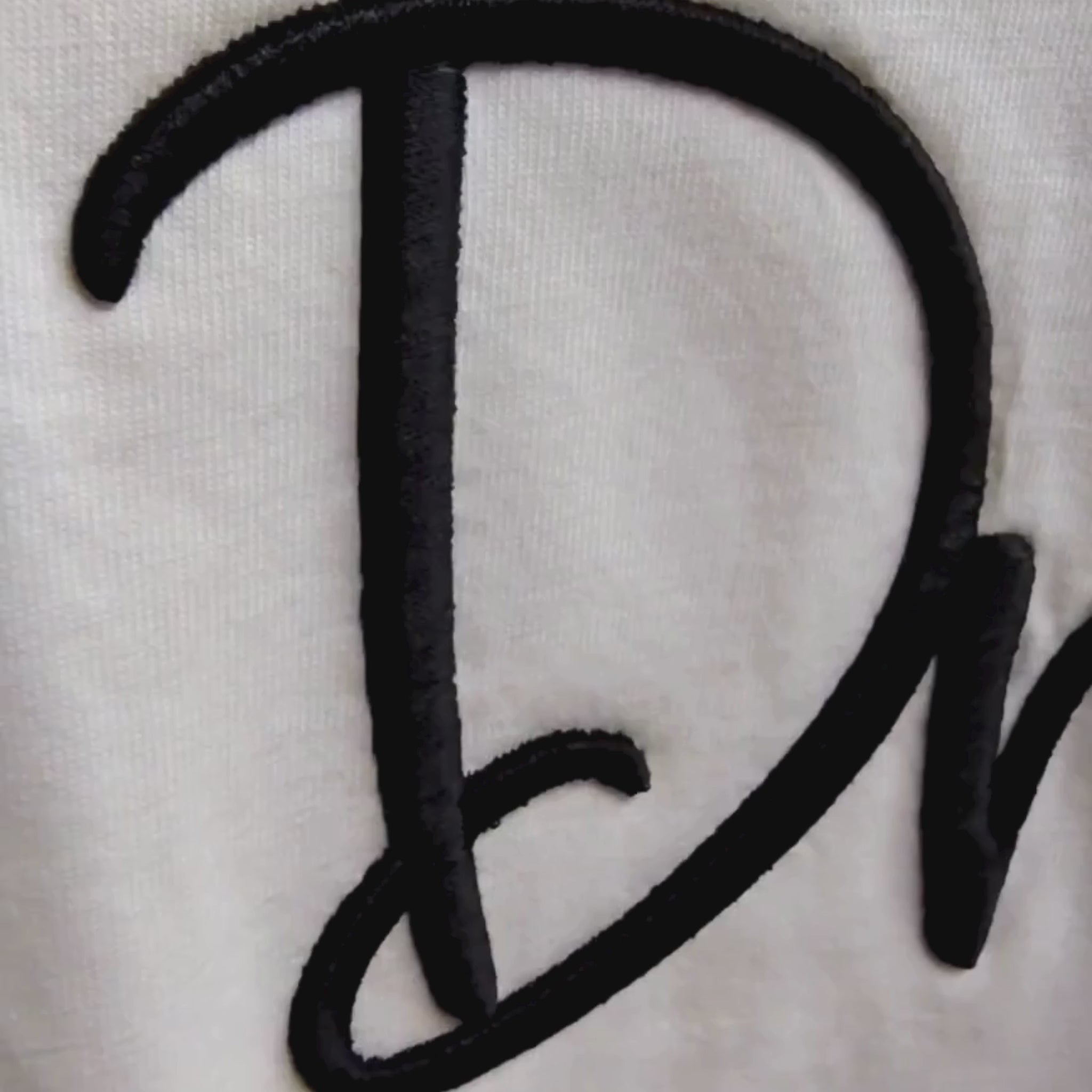 Video of 3D puff Dream embroidery detail — black raised cursive thread on cream fabric showing depth and texture, by Embroidist.