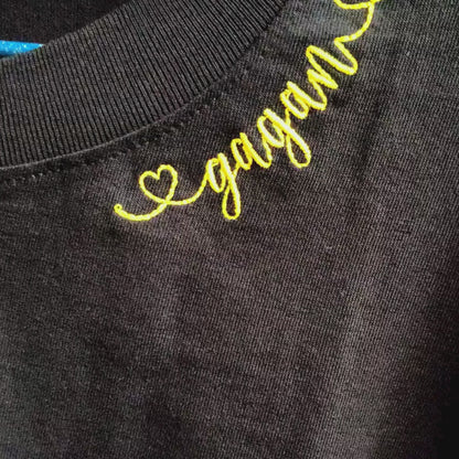 Video of personalised "♡gagan" name embroidery in gold cursive thread at neckline — close-up detail showing heart motif and script stitch on black fabric, by Embroidist.