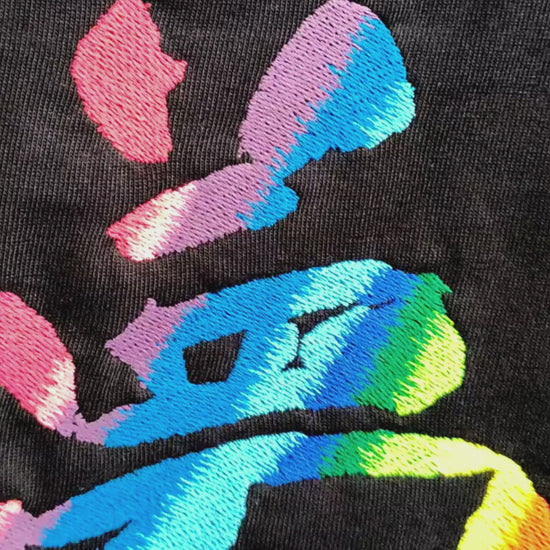 Video of 夢 Japanese kanji embroidery detail — 10-colour rainbow satin stitch on black fabric showing pink, blue, purple and green thread blending, back center placement, by Embroidist.