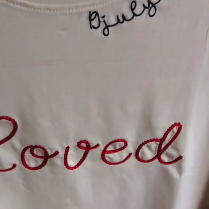 Close-up video of "Loved" chain stitch cursive embroidery detail — red looped thread texture on cream fabric, by Embroidist.