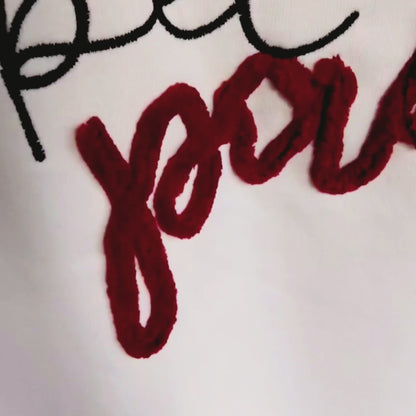 Close-up video of "pet parent" two-colour chenille embroidery detail — red and black fluffy thread texture on cream fabric, by Embroidist.