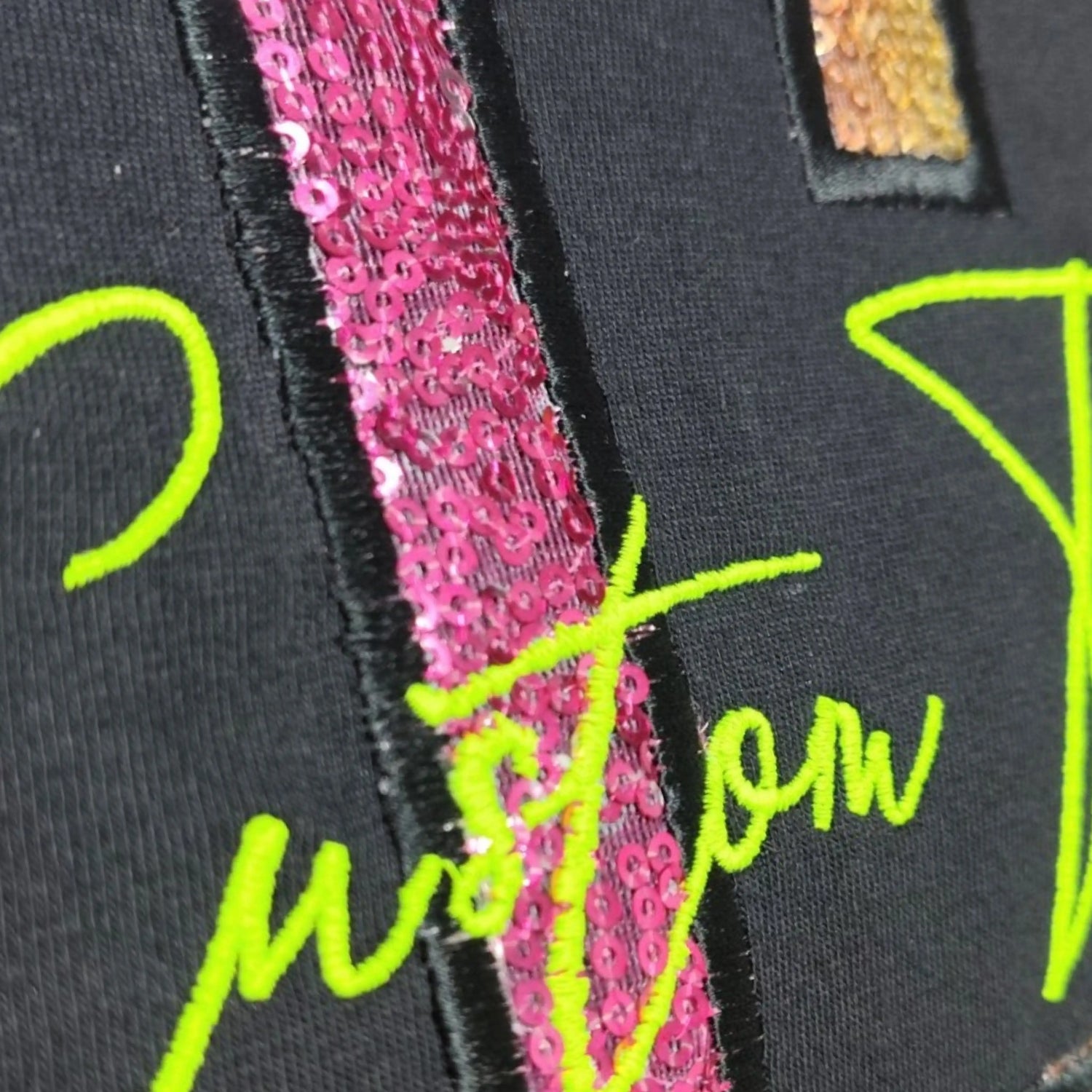 Close-up of sequin appliqué letter with neon lime green machine embroidered script on black tee — Embroidist