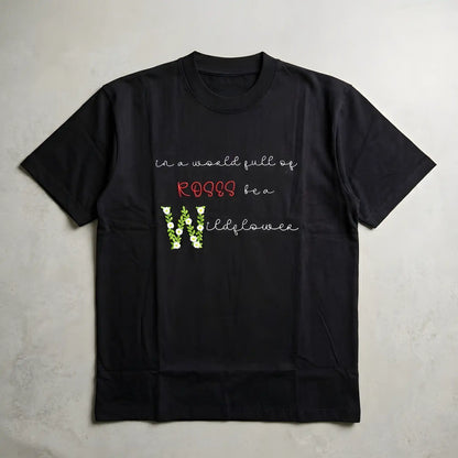 Wildflower floral embroidery t-shirt flatlay — "in a world full of roses be a wildflower" satin stitch floral lettering on black oversized tee, machine embroidered in India by Embroidist