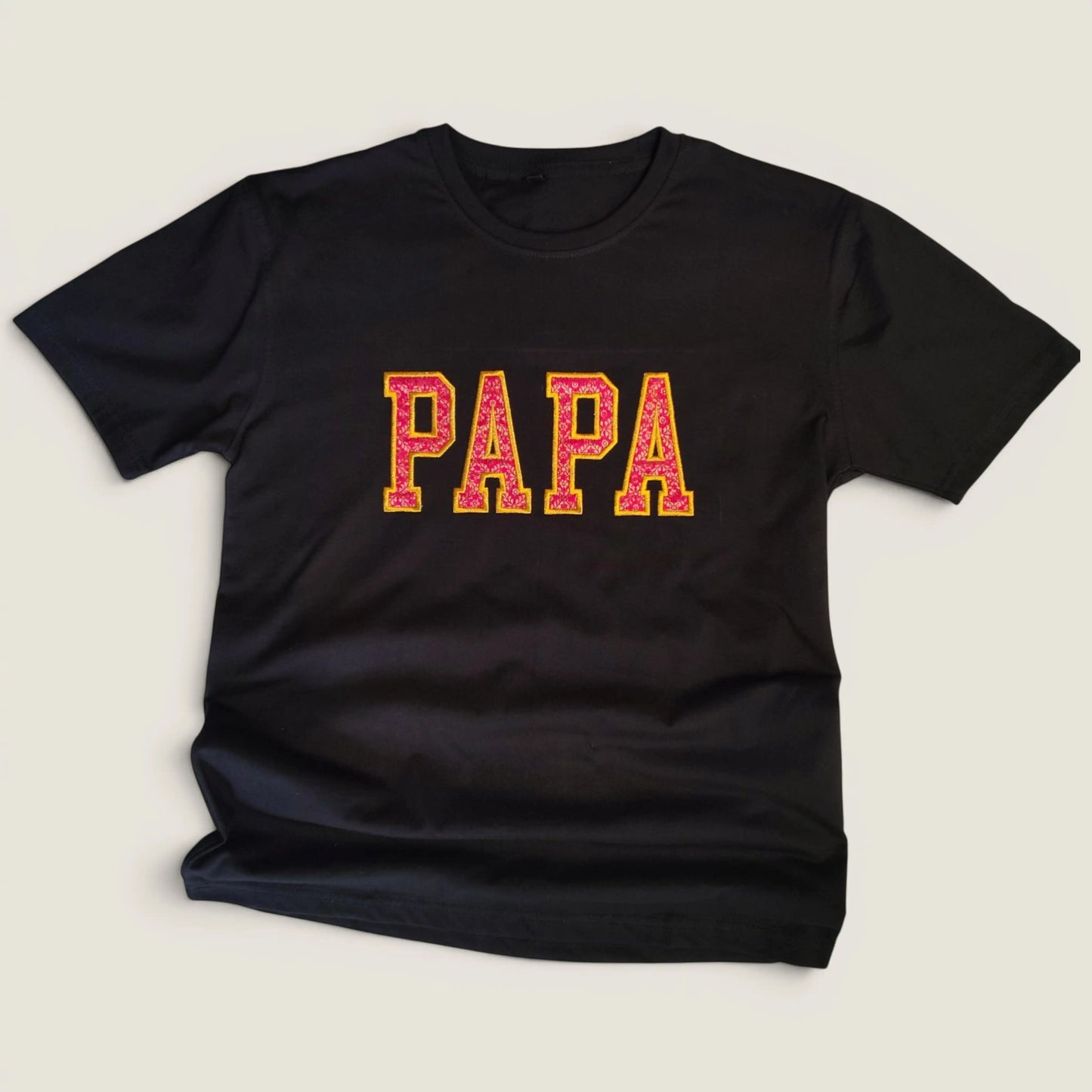 Flat lay of custom Zari embroidery t-shirt with PAPA in pink and gold varsity letters | Embroidist