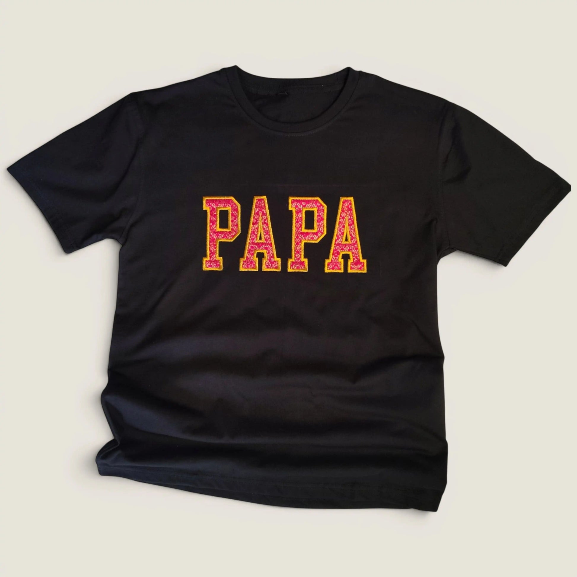 Flat lay of custom Zari embroidery t-shirt with PAPA in pink and gold varsity letters | Embroidist